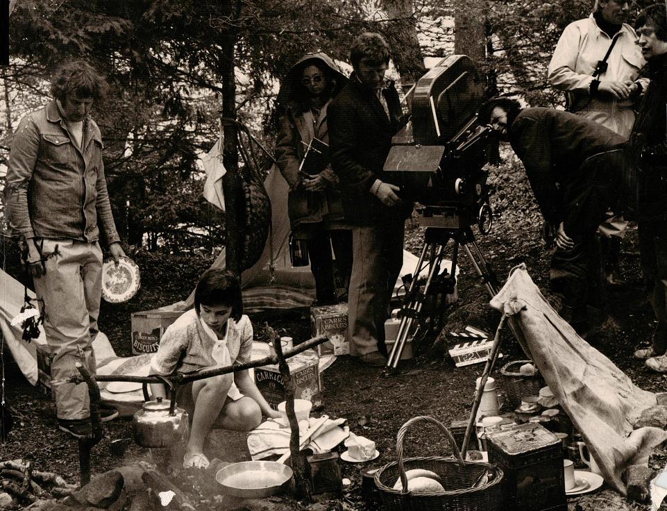 Suzanna Hamilton as The Mate Susan, cooking buttered eggs on the camp fire on Wild Cat Island. Director Claude Whatham, Sue Merry, Bobby Sitwell and DoP Denis Lewiston look on, clad in wet weather gear.
